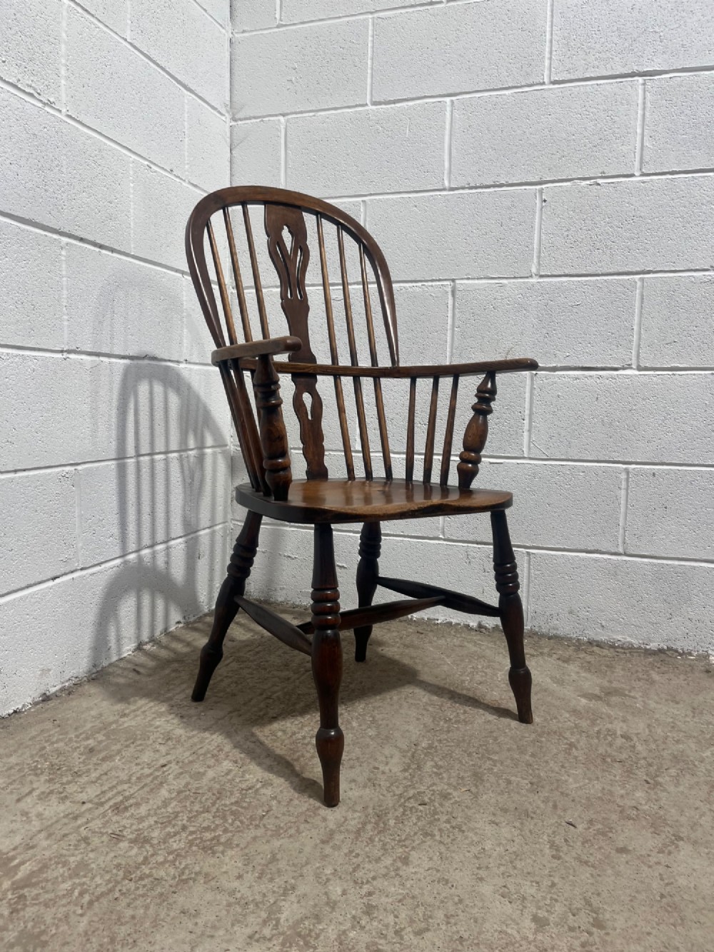 An antique 19th-century ash and elm high-back Windsor armchair featuring a hoop back with central pierced splat, turned arm supports, shaped saddle seat, and turned legs with an H-stretcher. View XI