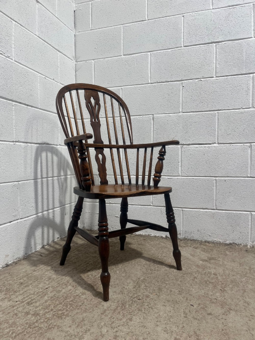 An antique 19th-century ash and elm high-back Windsor armchair featuring a hoop back with central pierced splat, turned arm supports, shaped saddle seat, and turned legs with an H-stretcher. View XIII