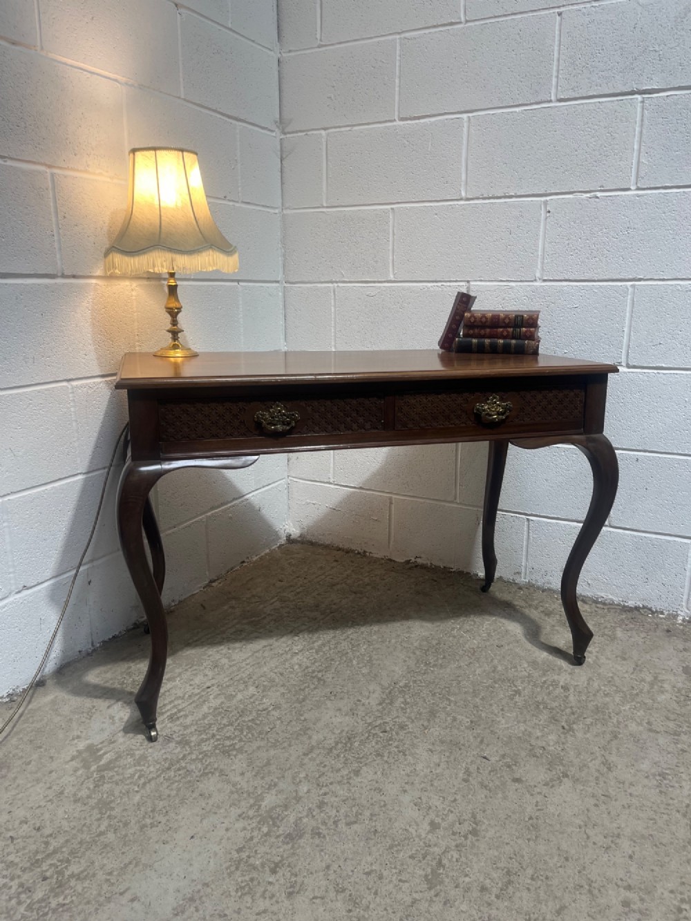 An Edwardian dark mahogany writing desk featuring two blind fretwork carved drawers with brass drop handles and slender cabriole legs on brass castors. View II