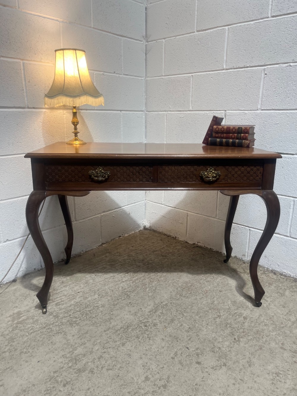 An Edwardian dark mahogany writing desk featuring two blind fretwork carved drawers with brass drop handles and slender cabriole legs on brass castors. View V