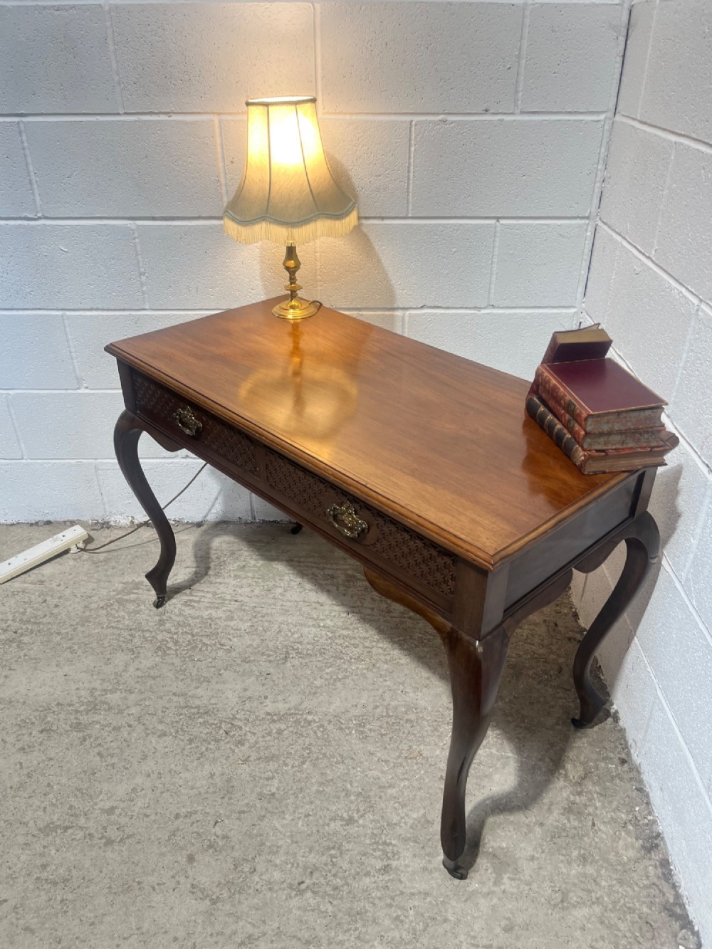 An Edwardian dark mahogany writing desk featuring two blind fretwork carved drawers with brass drop handles and slender cabriole legs on brass castors. View VII