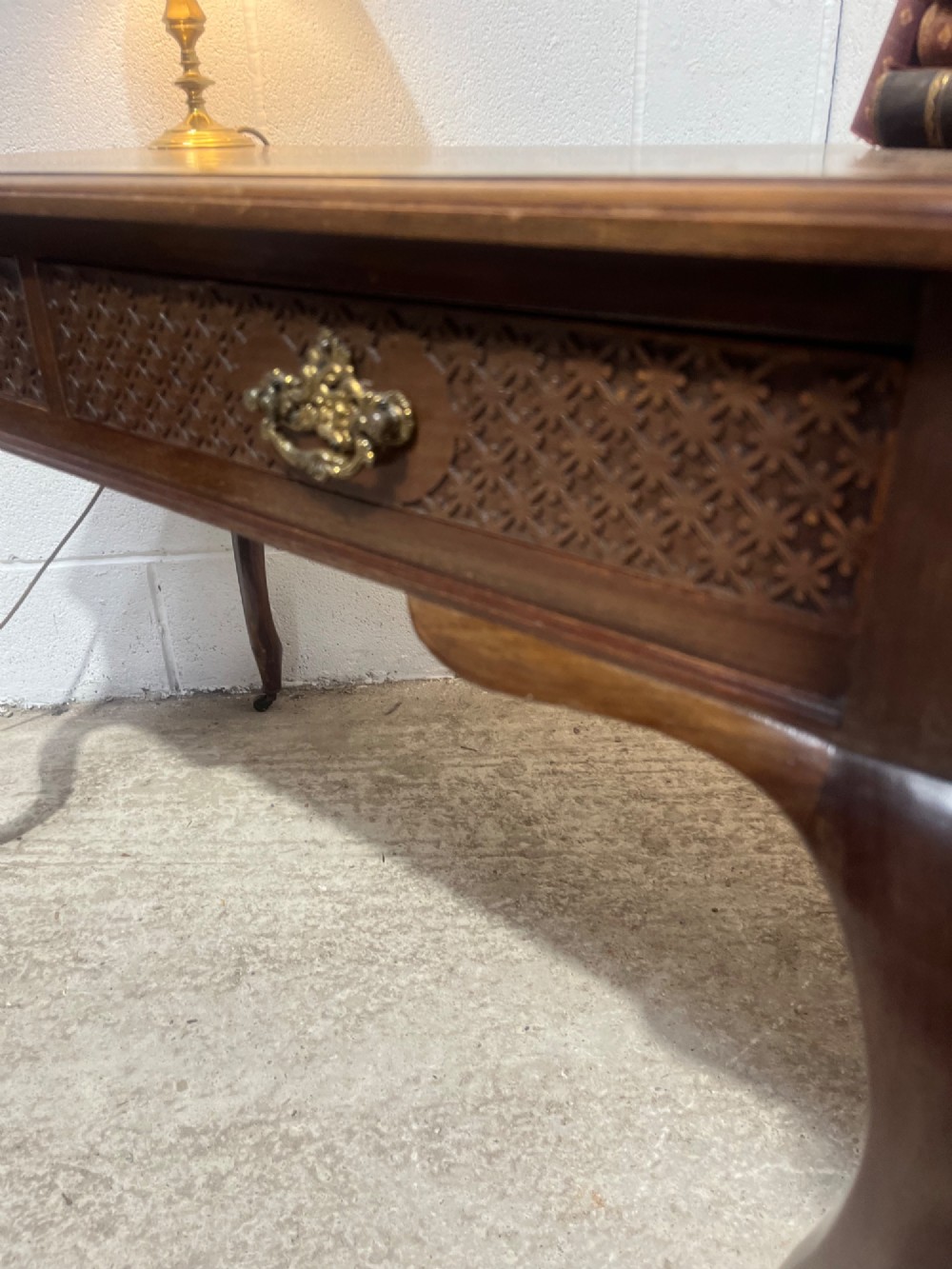 An Edwardian dark mahogany writing desk featuring two blind fretwork carved drawers with brass drop handles and slender cabriole legs on brass castors. View IX