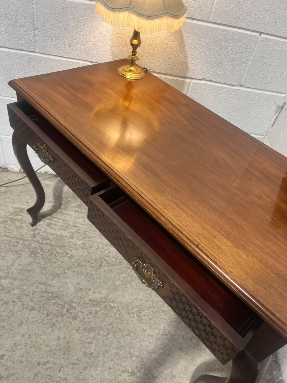 An Edwardian dark mahogany writing desk featuring two blind fretwork carved drawers with brass drop handles and slender cabriole legs on brass castors. View XI