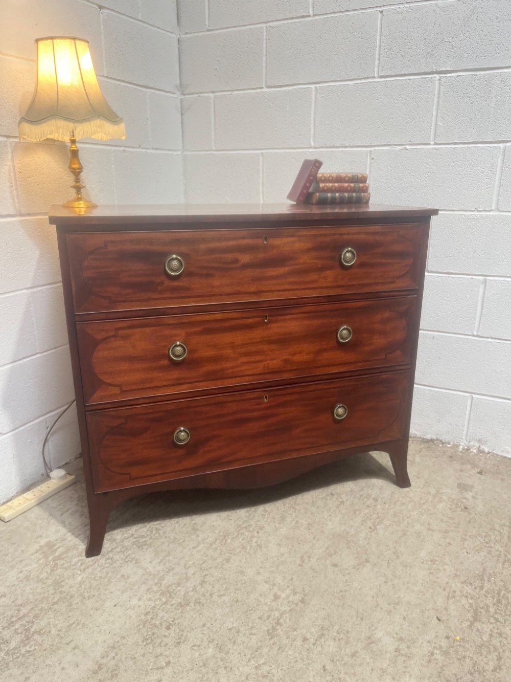 A nineteenth-century mahogany chest of three full-width drawers featuring brass ring handles, boxwood string inlay, and splayed bracket feet.
