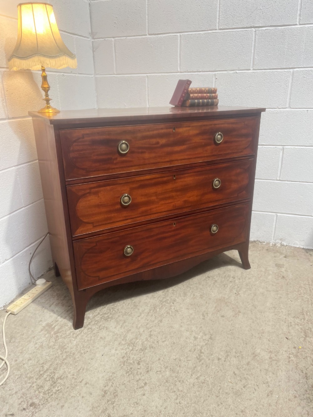 A nineteenth-century mahogany chest of three full-width drawers featuring brass ring handles, boxwood string inlay, and splayed bracket feet. View III