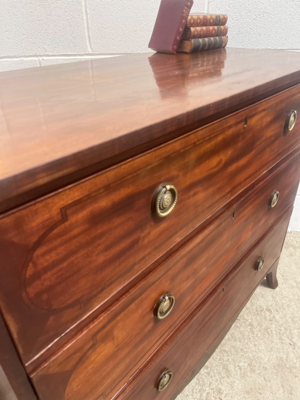 A nineteenth-century mahogany chest of three full-width drawers featuring brass ring handles, boxwood string inlay, and splayed bracket feet. View V