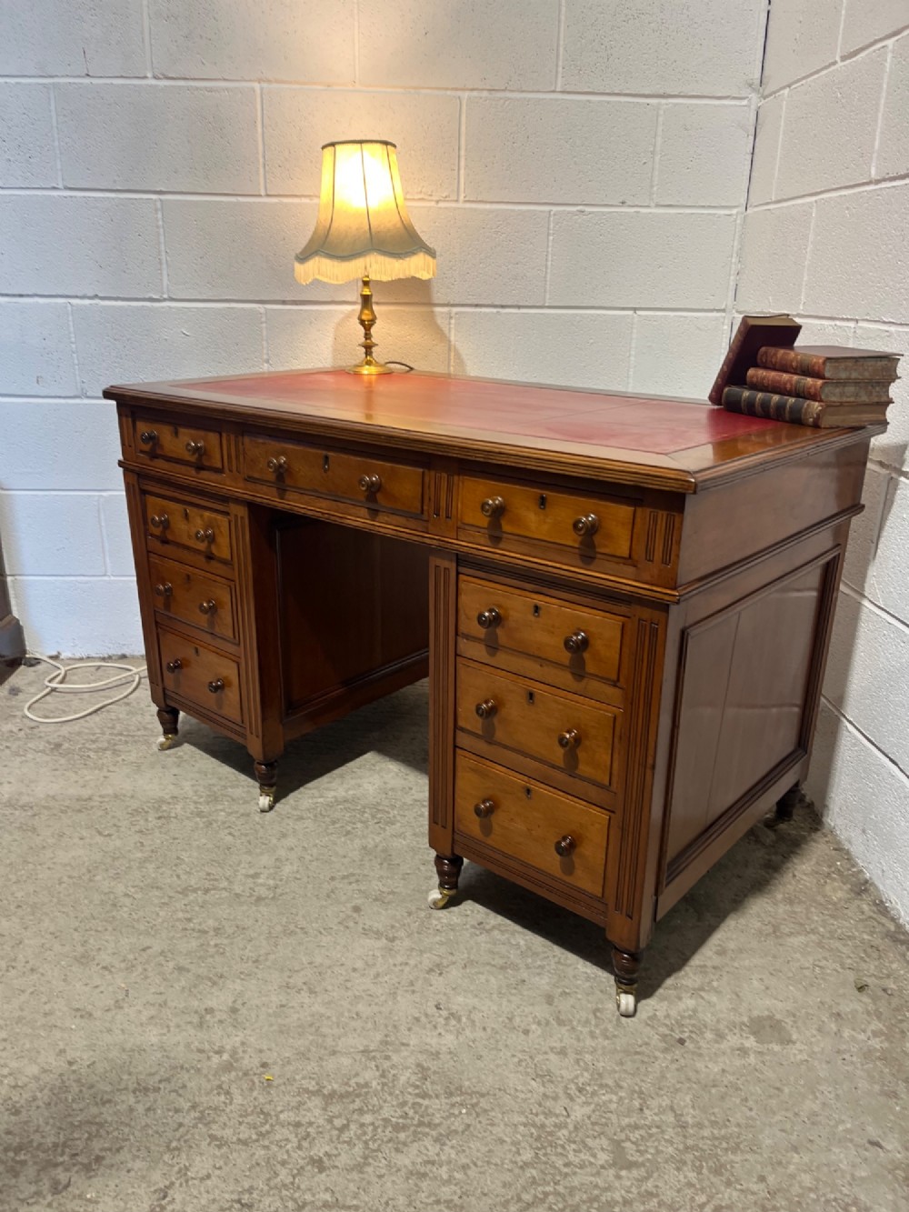 A 19th-century mahogany free-standing pedestal desk featuring a red leather top inset, multiple drawers with turned knobs, and brass castors. View II