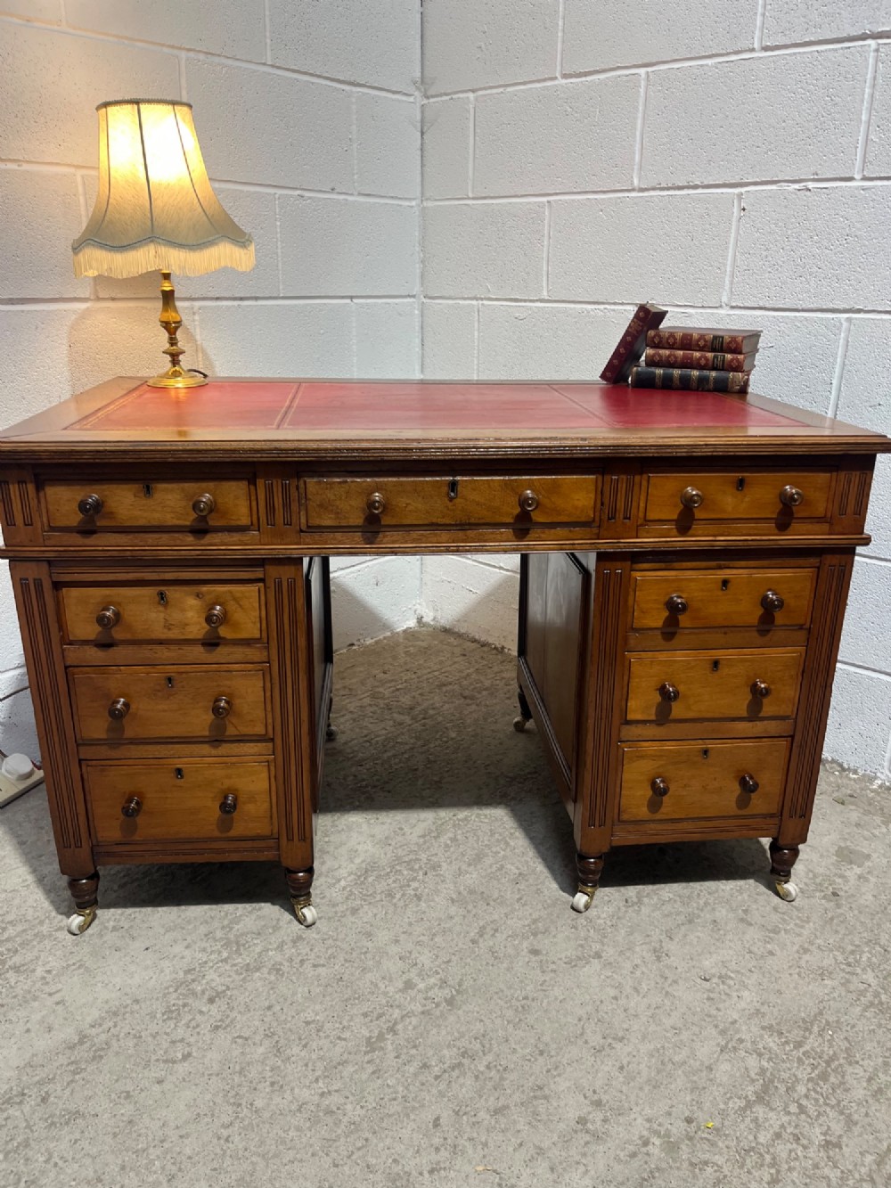 A 19th-century mahogany free-standing pedestal desk featuring a red leather top inset, multiple drawers with turned knobs, and brass castors. View V