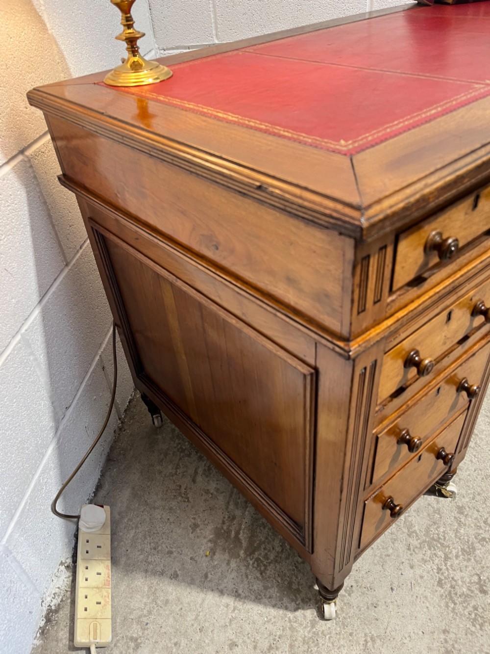 A 19th-century mahogany free-standing pedestal desk featuring a red leather top inset, multiple drawers with turned knobs, and brass castors. View VI