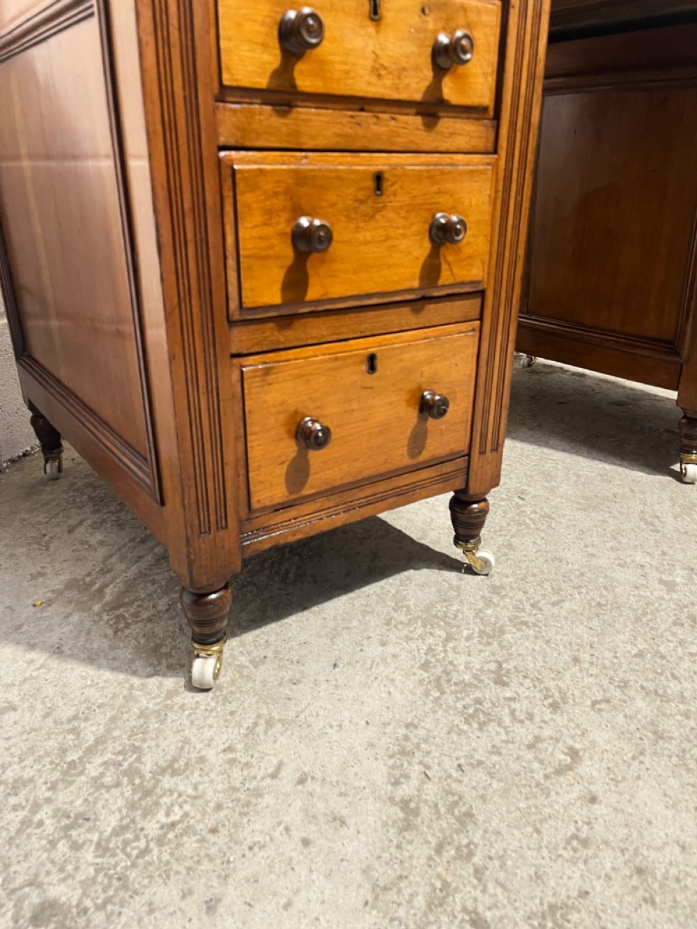 A 19th-century mahogany free-standing pedestal desk featuring a red leather top inset, multiple drawers with turned knobs, and brass castors. View VII