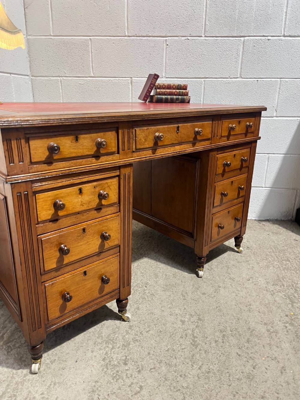 A 19th-century mahogany free-standing pedestal desk featuring a red leather top inset, multiple drawers with turned knobs, and brass castors. View VIII