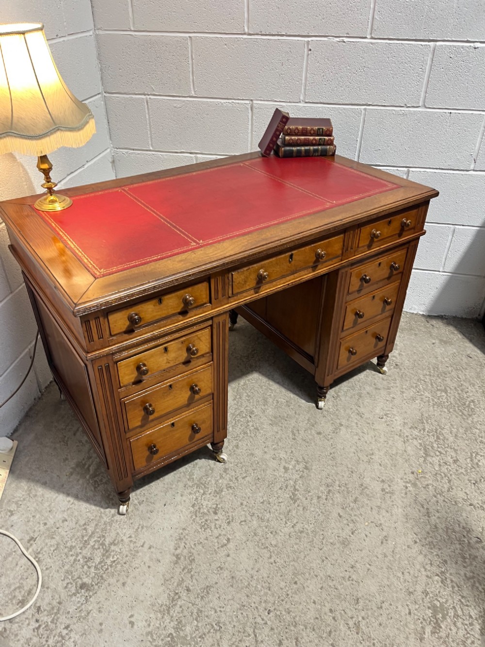 A 19th-century mahogany free-standing pedestal desk featuring a red leather top inset, multiple drawers with turned knobs, and brass castors. View IX