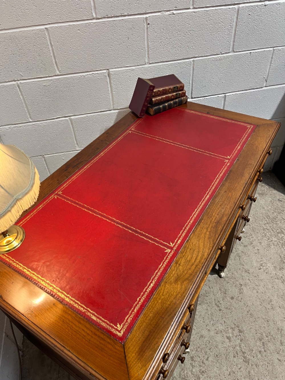 A 19th-century mahogany free-standing pedestal desk featuring a red leather top inset, multiple drawers with turned knobs, and brass castors. View X