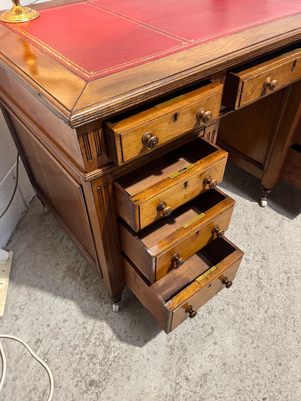 A 19th-century mahogany free-standing pedestal desk featuring a red leather top inset, multiple drawers with turned knobs, and brass castors. View XIII