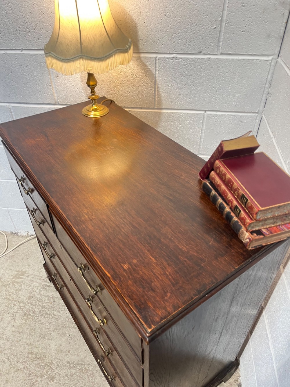 An antique Georgian dark oak chest of drawers with two short drawers above three long drawers, featuring brass swan-neck handles and bracket feet. View VI
