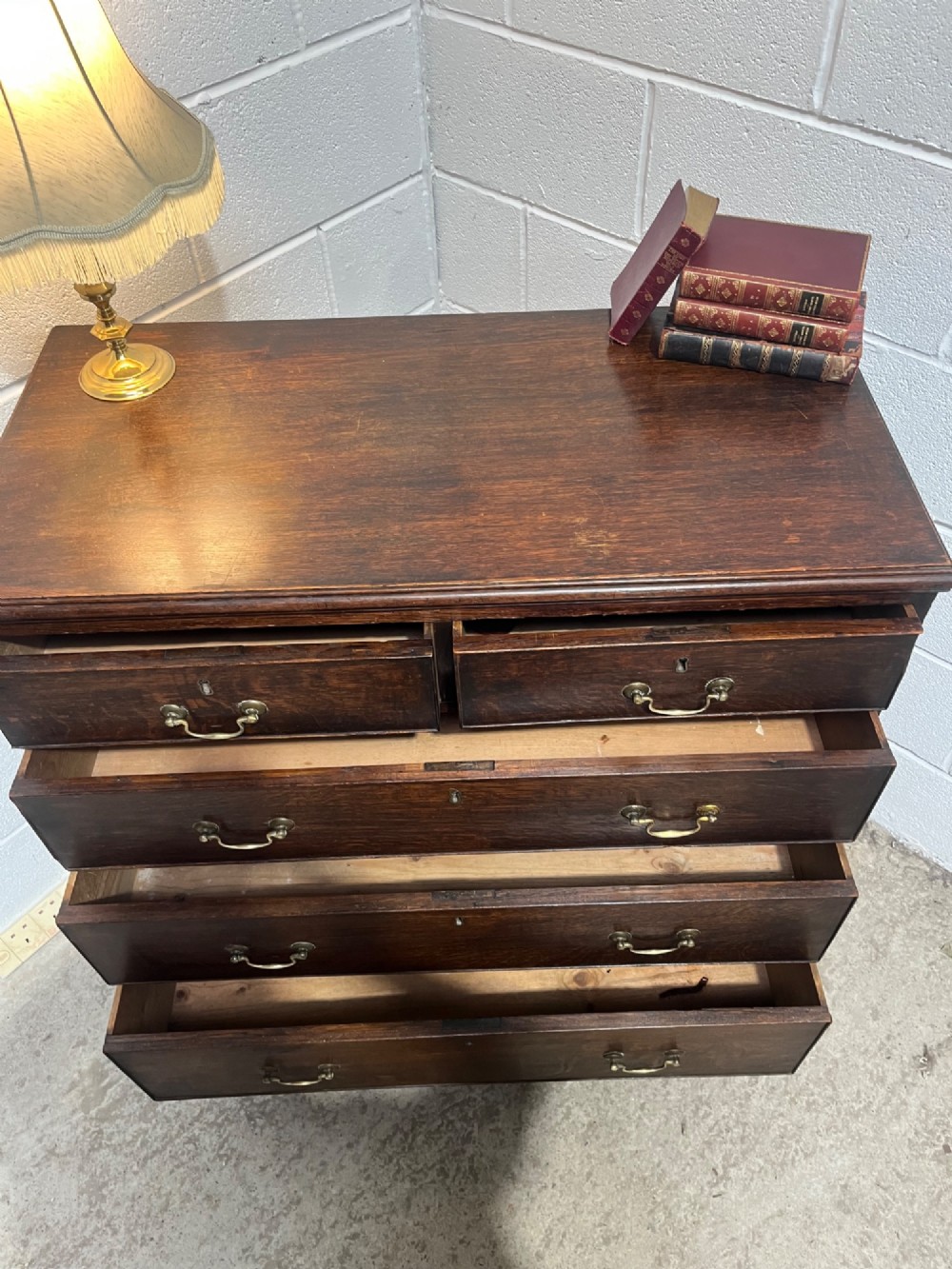 An antique Georgian dark oak chest of drawers with two short drawers above three long drawers, featuring brass swan-neck handles and bracket feet. View IX