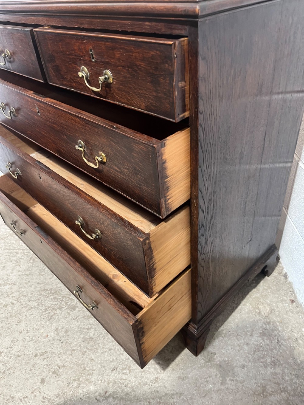 An antique Georgian dark oak chest of drawers with two short drawers above three long drawers, featuring brass swan-neck handles and bracket feet. View X