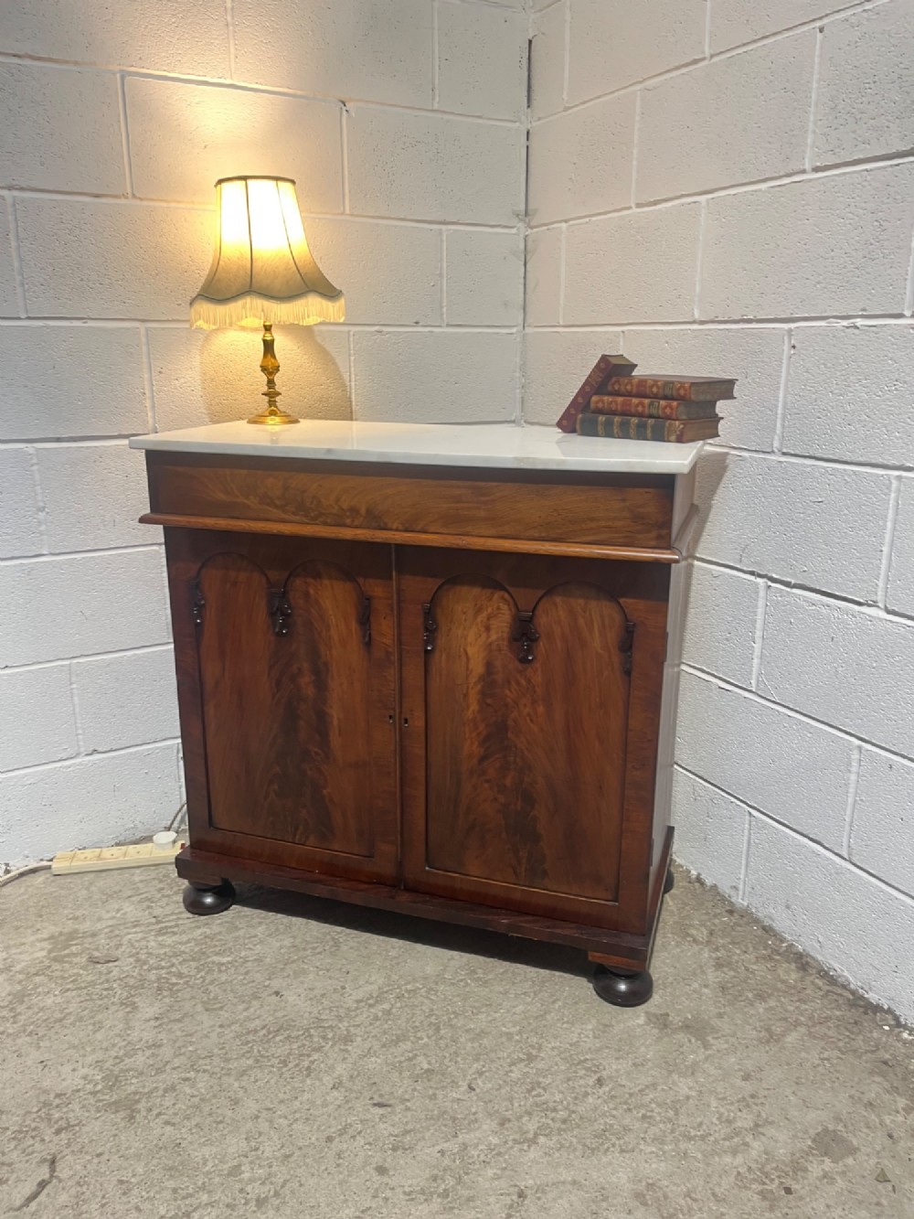 A 19th-century mahogany cupboard featuring twin arched panel doors, flattened bun feet, and a fitted white marble top.