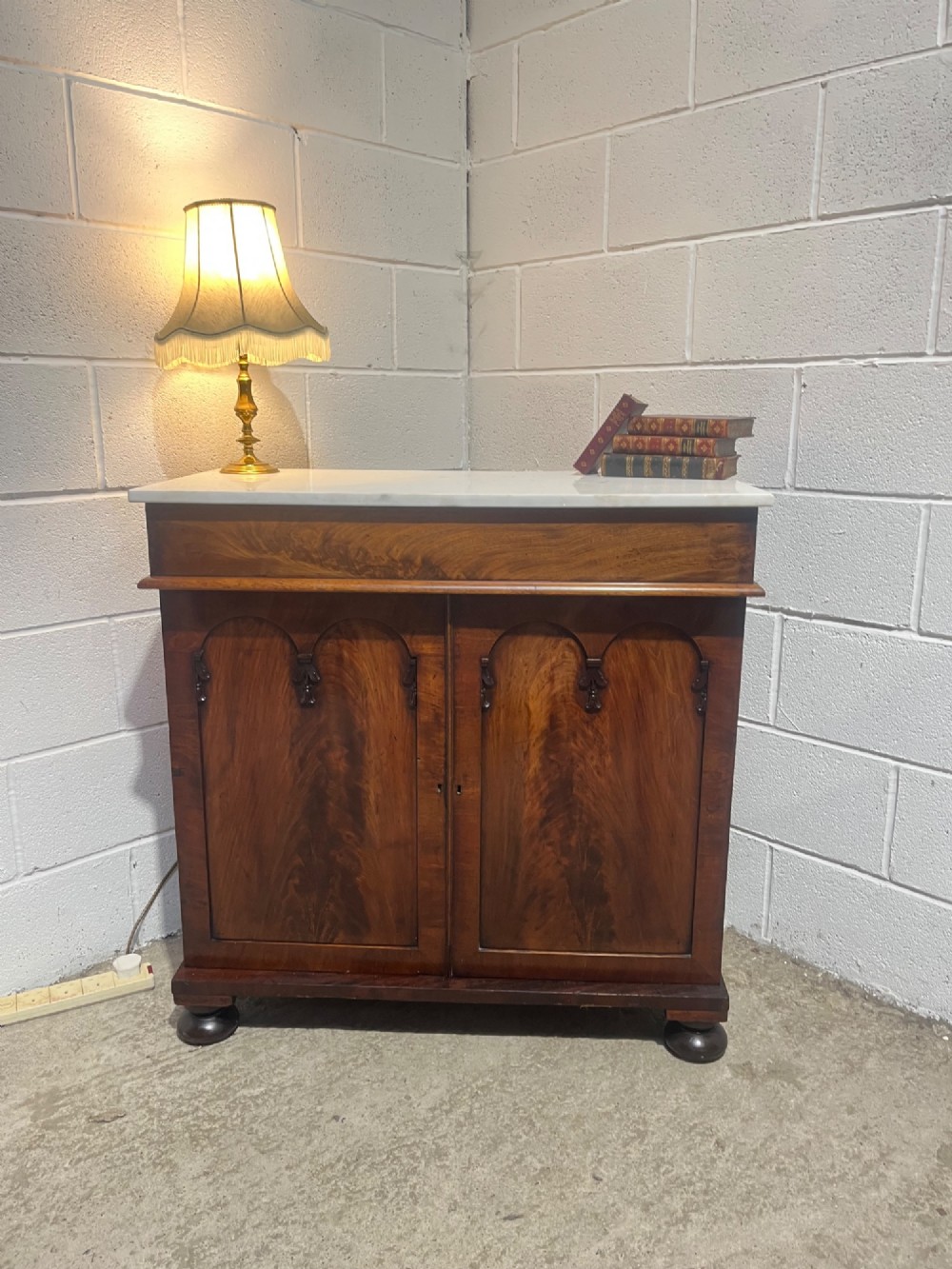 A 19th-century mahogany cupboard featuring twin arched panel doors, flattened bun feet, and a fitted white marble top. View II