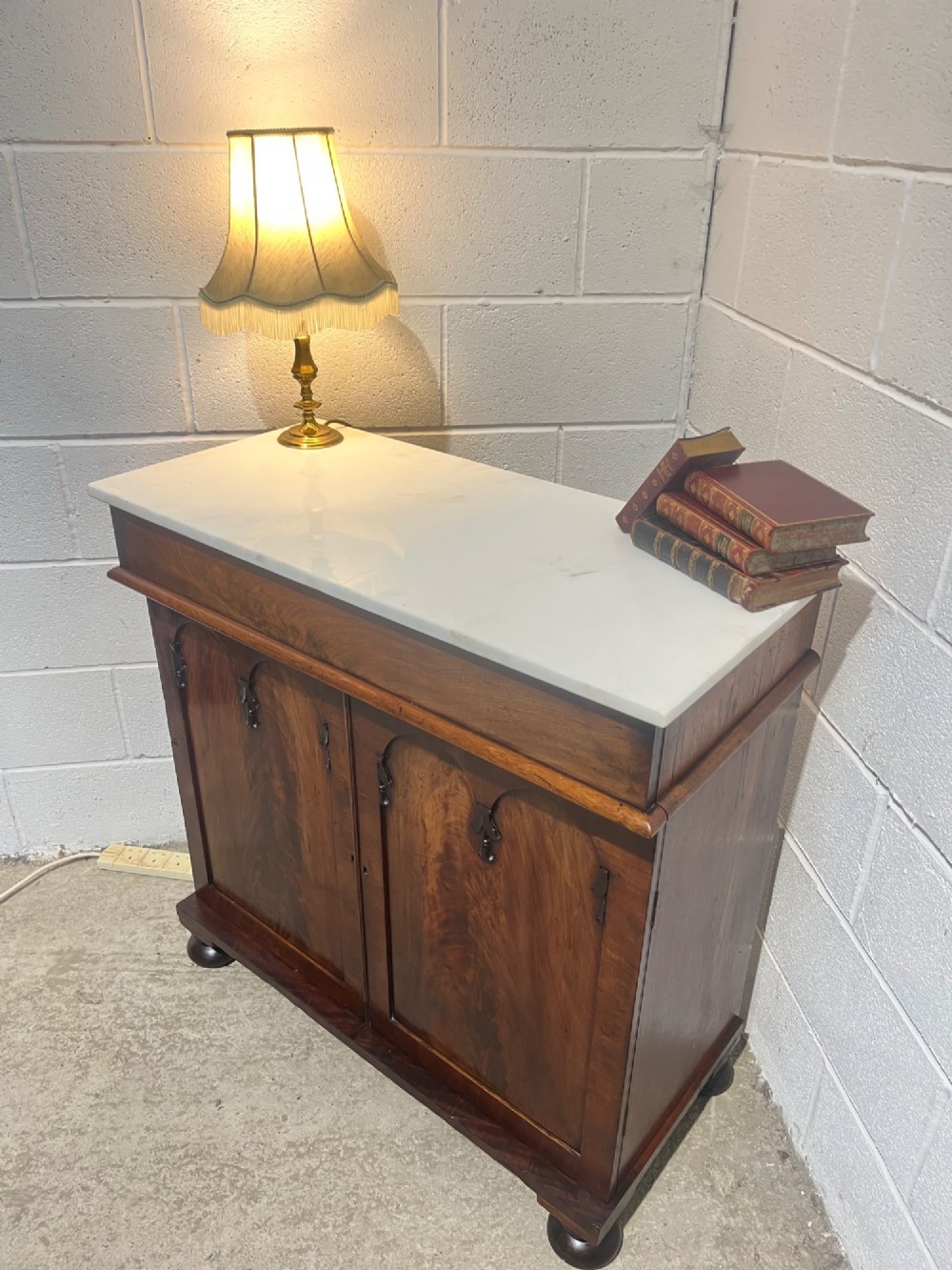 A 19th-century mahogany cupboard featuring twin arched panel doors, flattened bun feet, and a fitted white marble top. View IV