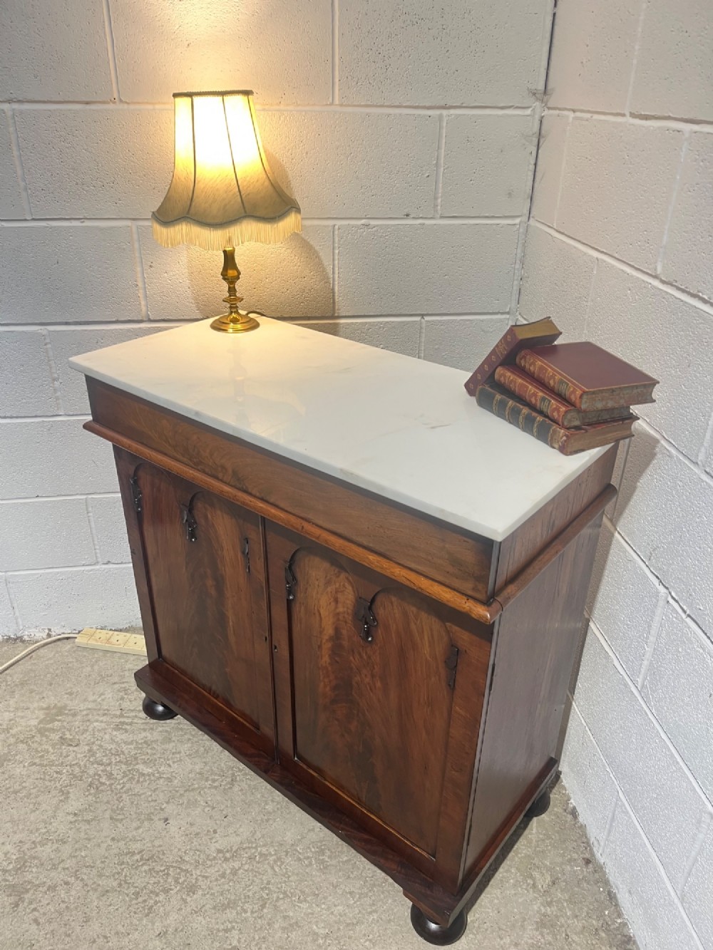 A 19th-century mahogany cupboard featuring twin arched panel doors, flattened bun feet, and a fitted white marble top. View V