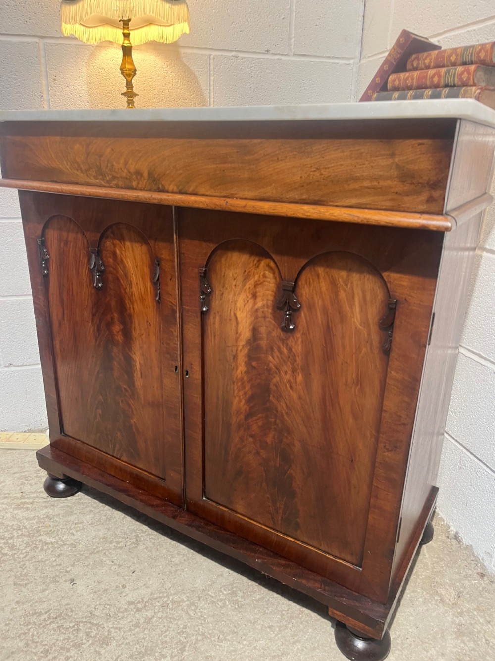 A 19th-century mahogany cupboard featuring twin arched panel doors, flattened bun feet, and a fitted white marble top. View VI