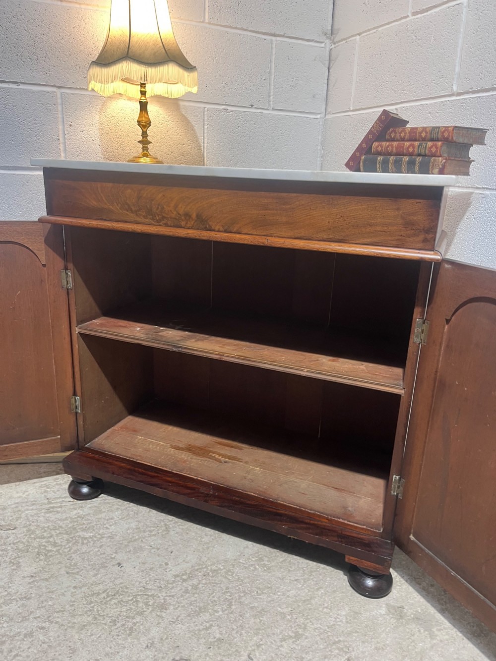A 19th-century mahogany cupboard featuring twin arched panel doors, flattened bun feet, and a fitted white marble top. View X