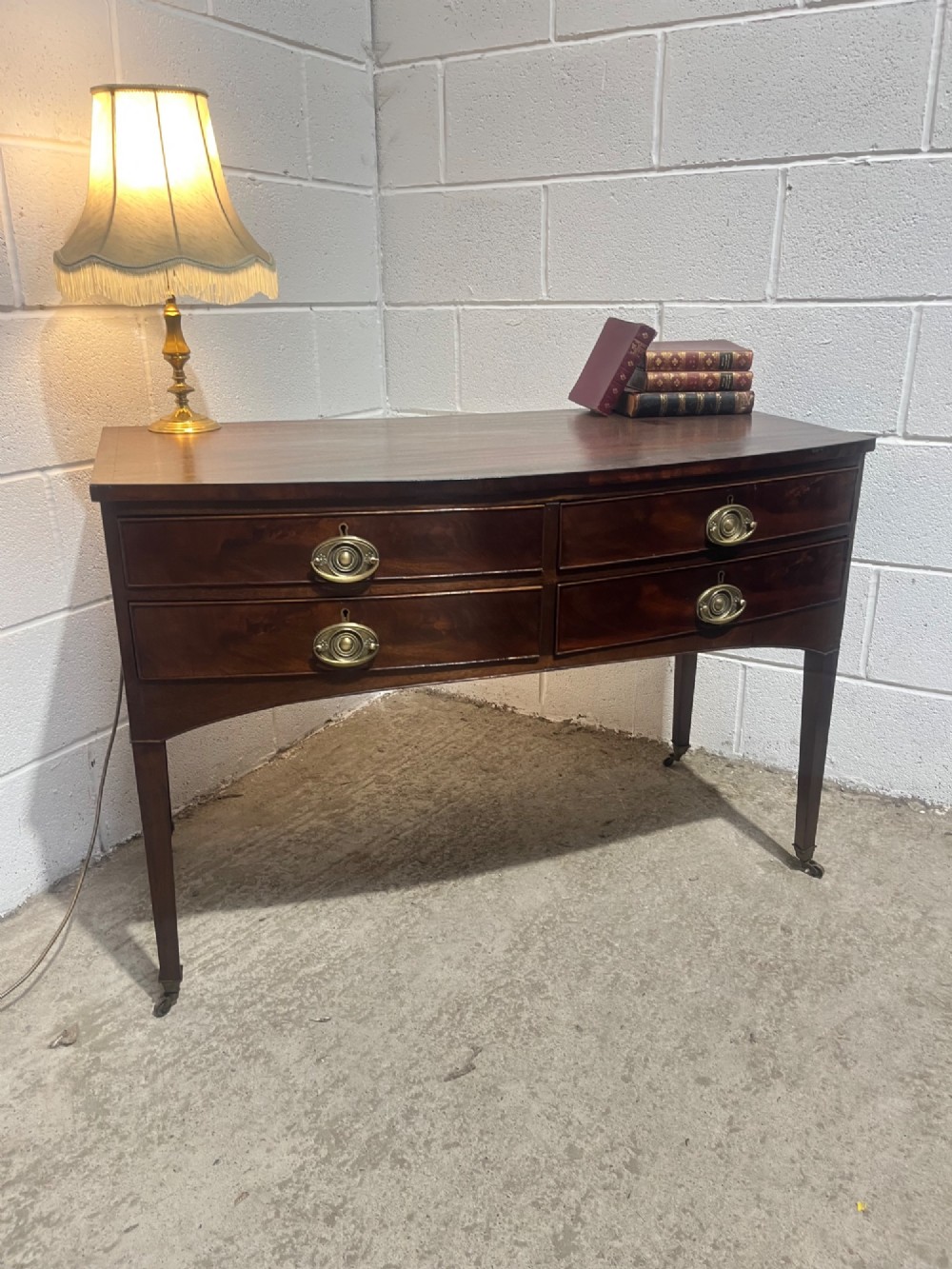 A Georgian mahogany bowfront hall table featuring four drawers with brass handles and tapered square legs on brass castors. View II