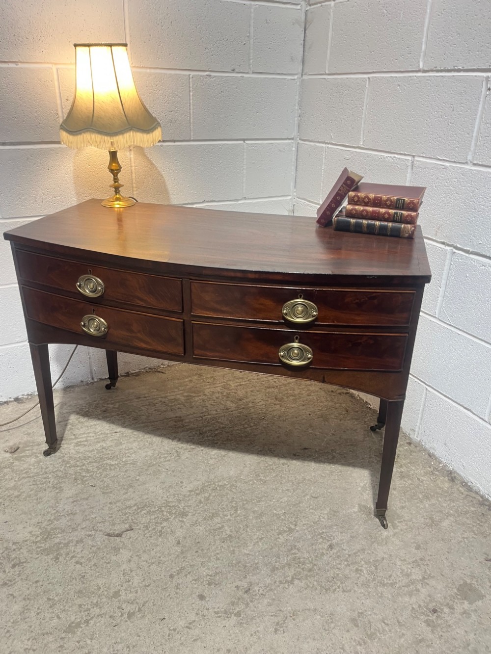 A Georgian mahogany bowfront hall table featuring four drawers with brass handles and tapered square legs on brass castors. View III