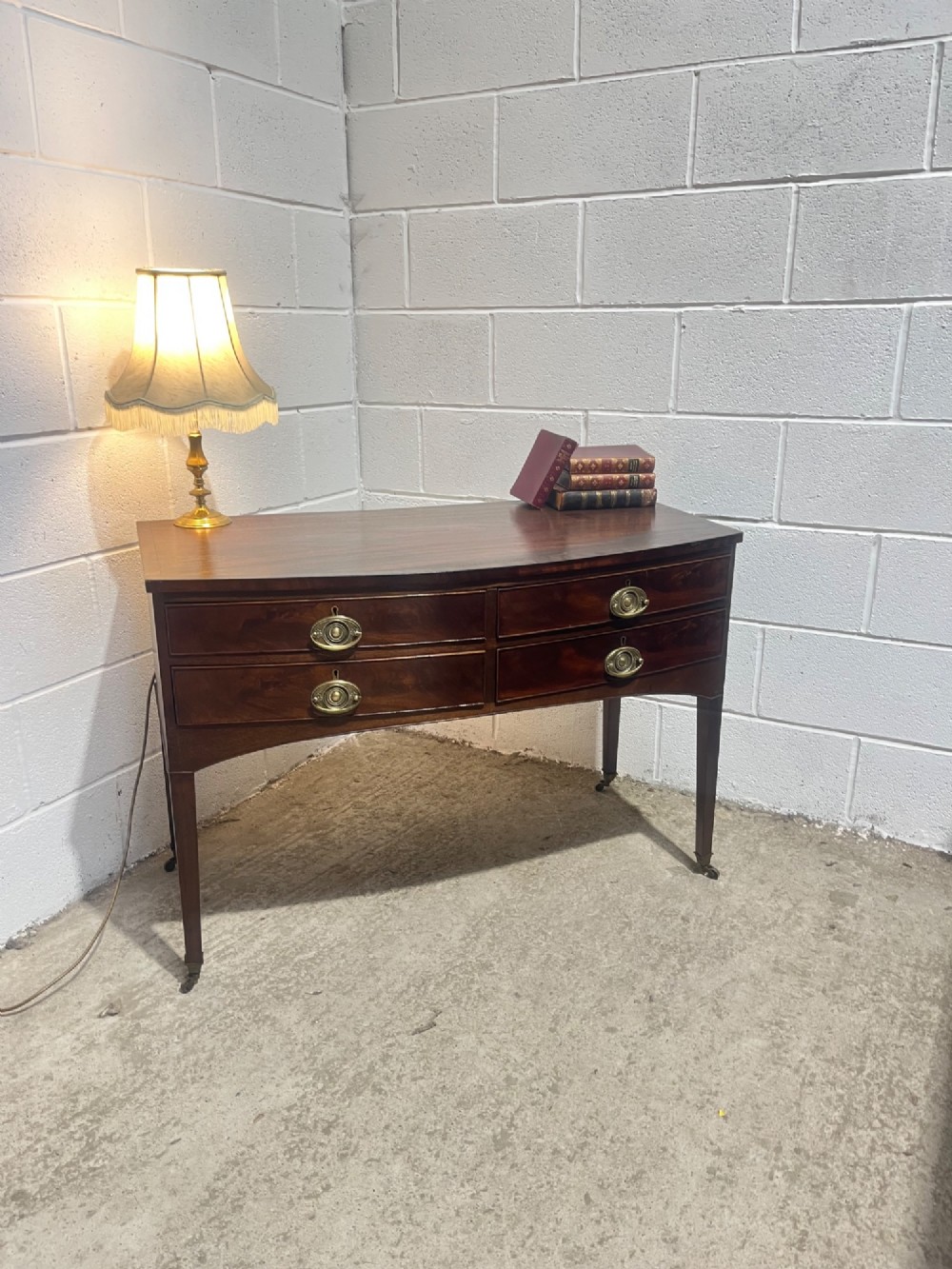 A Georgian mahogany bowfront hall table featuring four drawers with brass handles and tapered square legs on brass castors. View IV