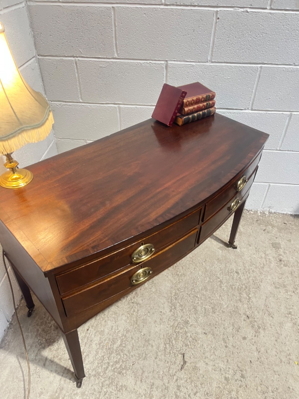 A Georgian mahogany bowfront hall table featuring four drawers with brass handles and tapered square legs on brass castors. View V