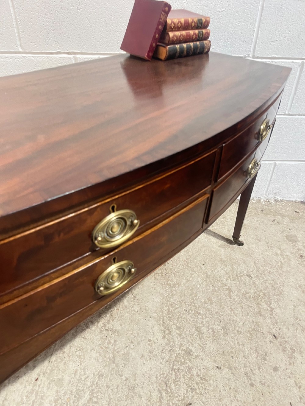 A Georgian mahogany bowfront hall table featuring four drawers with brass handles and tapered square legs on brass castors. View VI