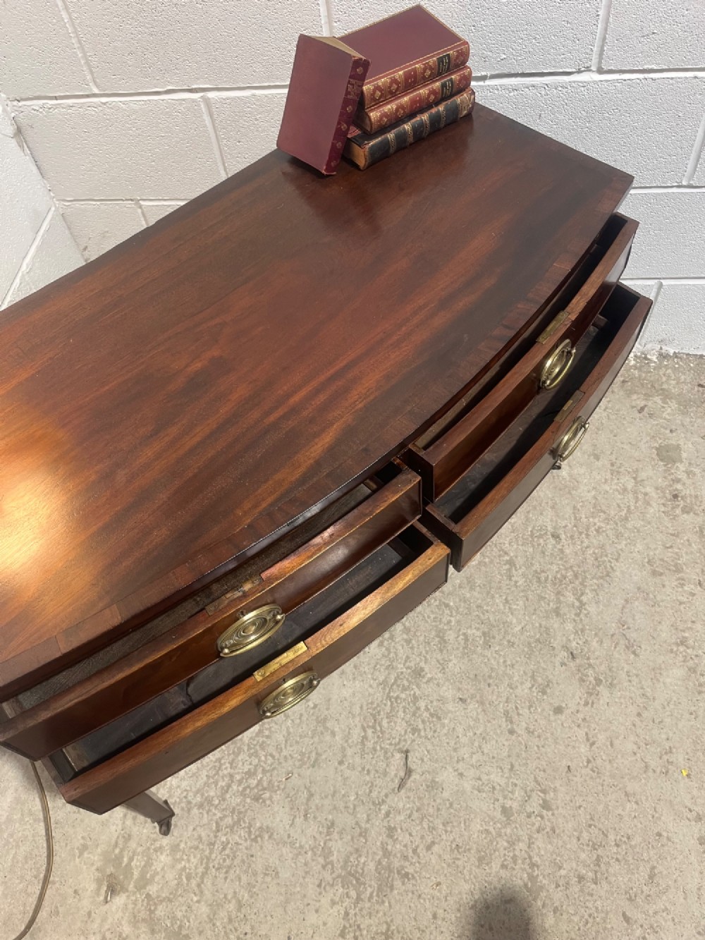 A Georgian mahogany bowfront hall table featuring four drawers with brass handles and tapered square legs on brass castors. View IX