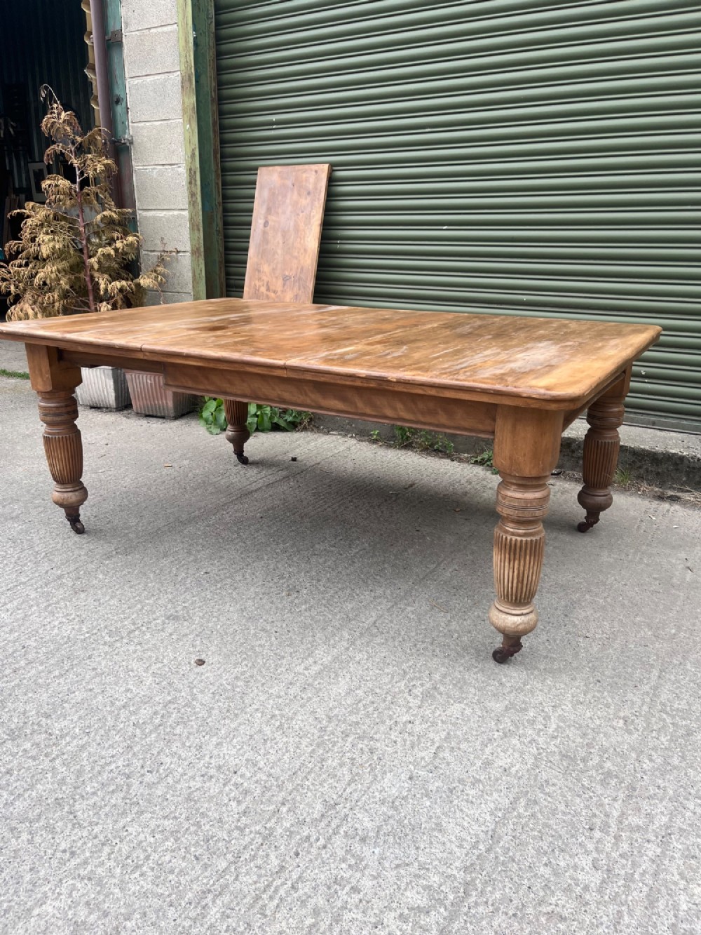 An antique 19th-century pine wind-out extending dining table with turned legs and metal castors.