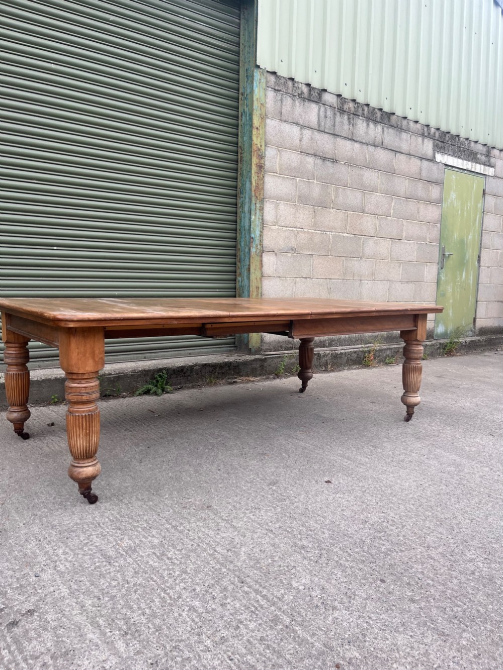 An antique 19th-century pine wind-out extending dining table with turned legs and metal castors. View II