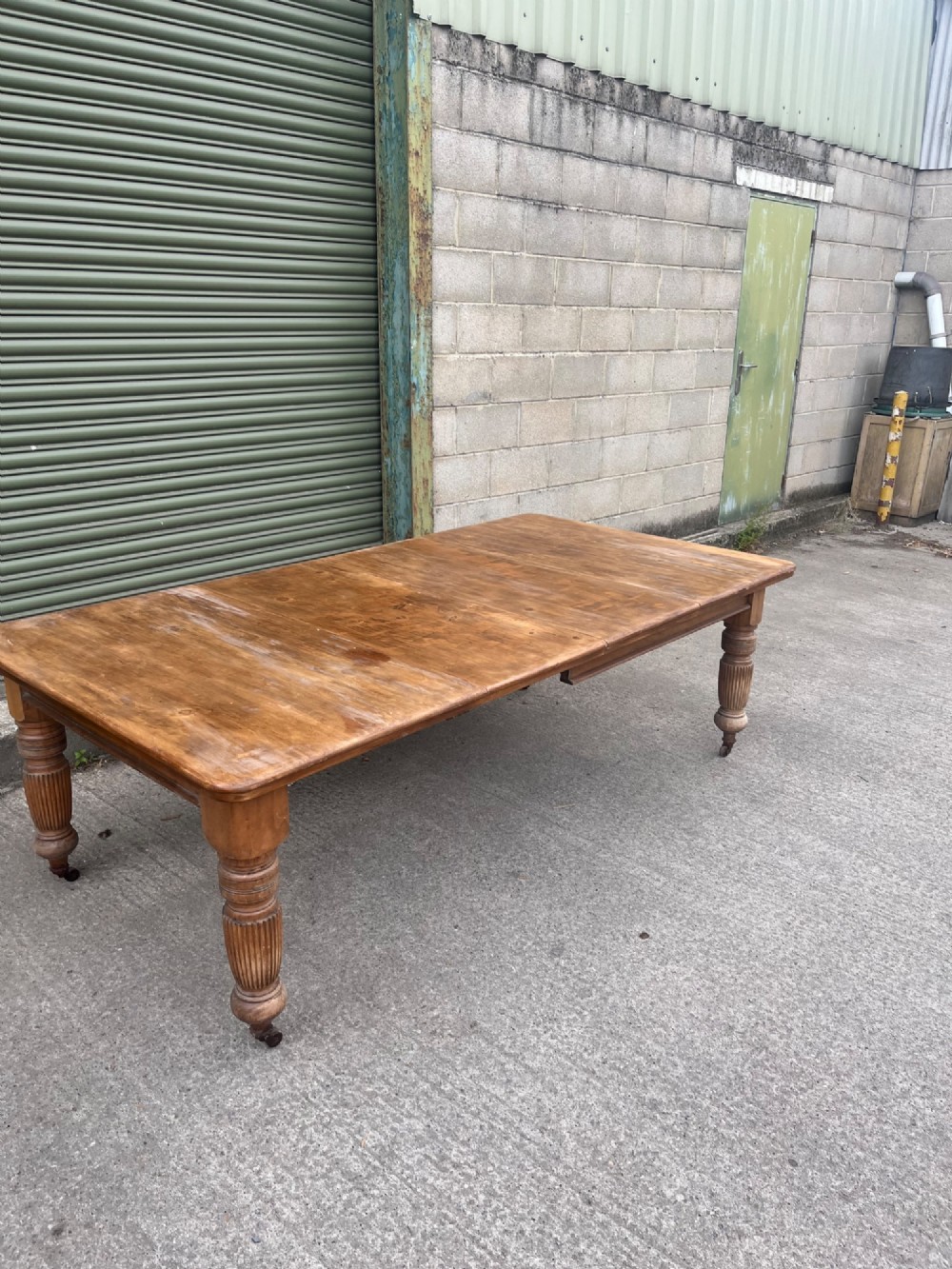 An antique 19th-century pine wind-out extending dining table with turned legs and metal castors. View III