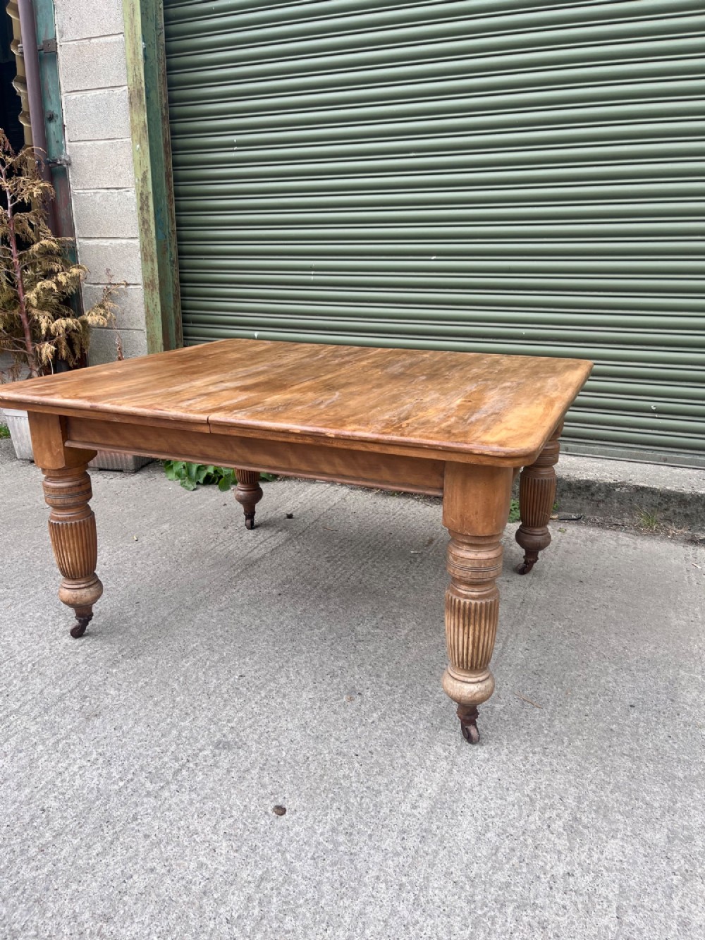 An antique 19th-century pine wind-out extending dining table with turned legs and metal castors. View X