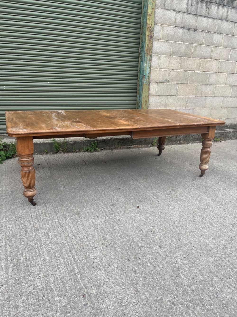 An antique 19th-century pine wind-out extending dining table with turned legs and metal castors. View XI