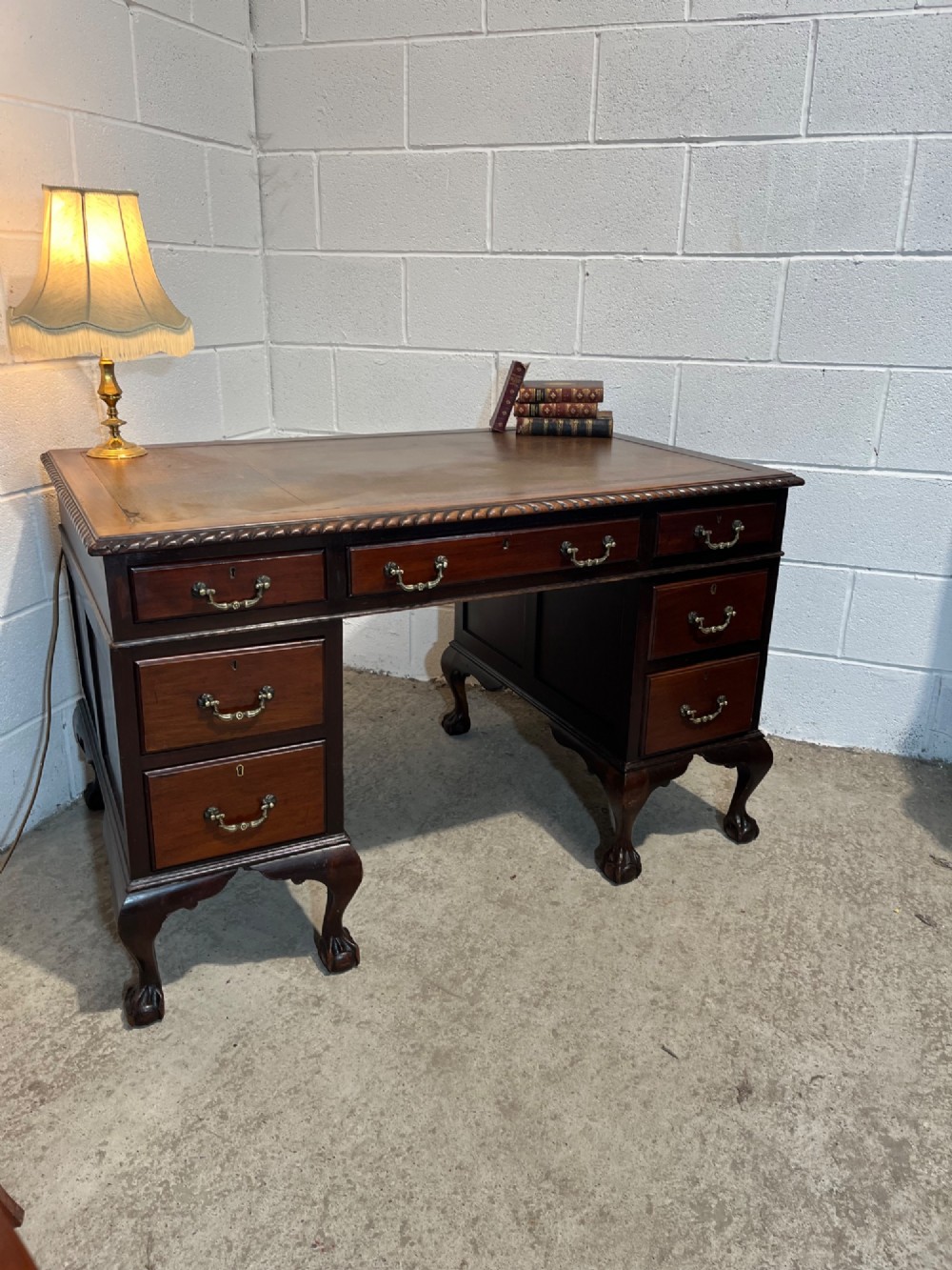 An early 20th-century dark mahogany pedestal writing desk featuring an inset leather top, brass swan-neck handles, seven drawers, and cabriole legs with ball and claw feet. View II