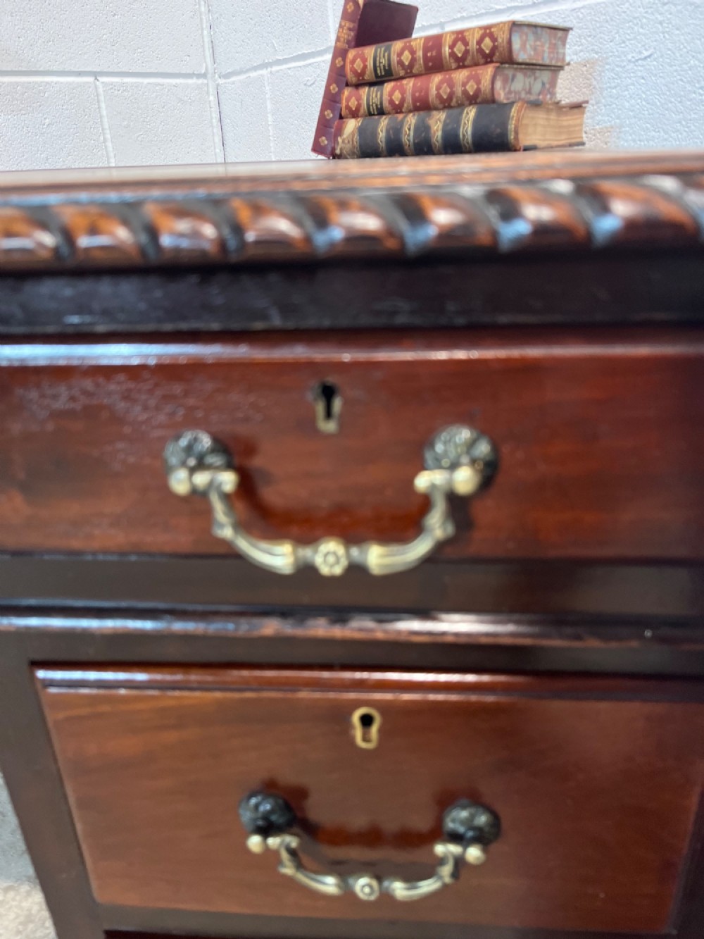 An early 20th-century dark mahogany pedestal writing desk featuring an inset leather top, brass swan-neck handles, seven drawers, and cabriole legs with ball and claw feet. View V