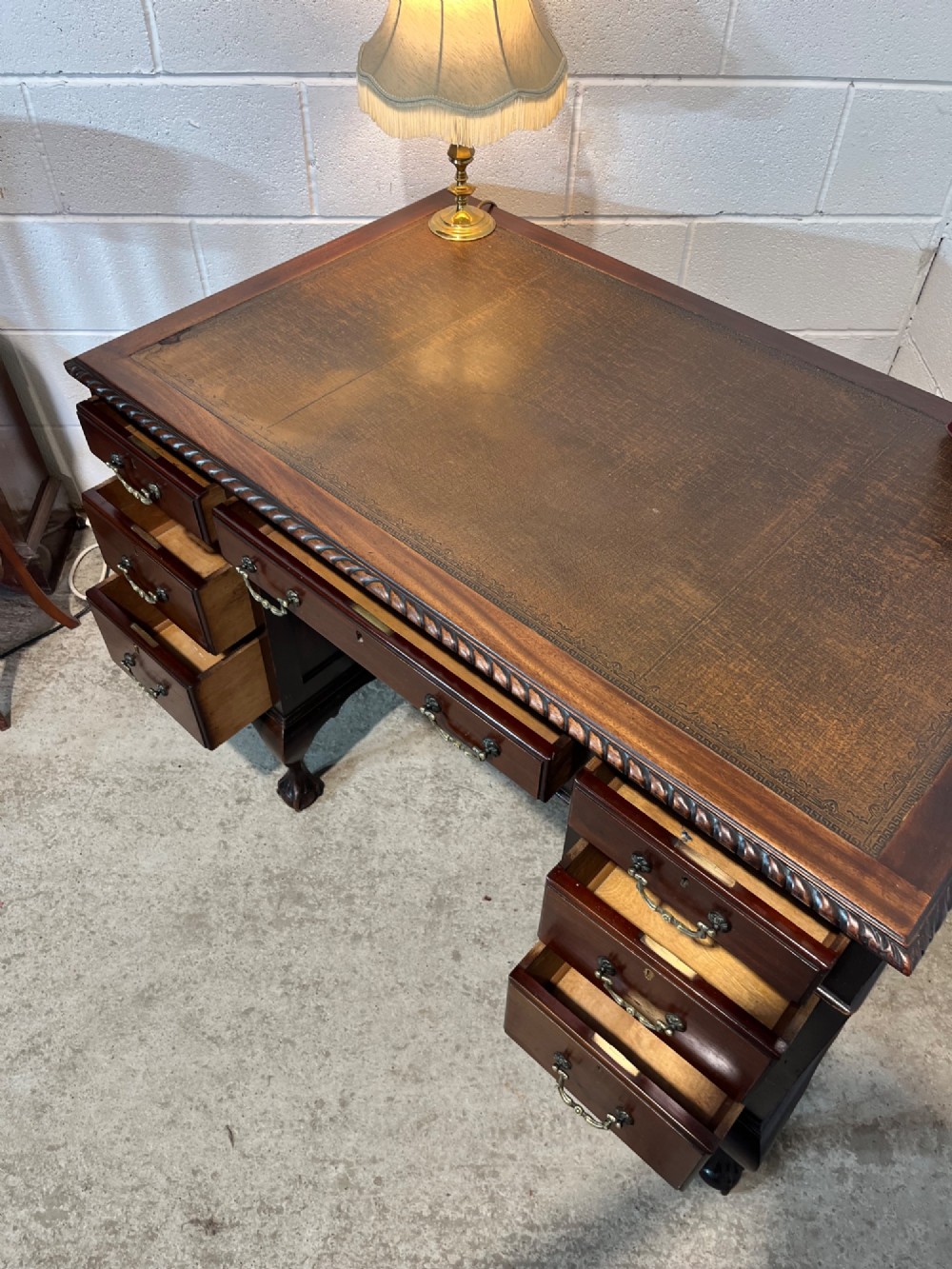 An early 20th-century dark mahogany pedestal writing desk featuring an inset leather top, brass swan-neck handles, seven drawers, and cabriole legs with ball and claw feet. View IX