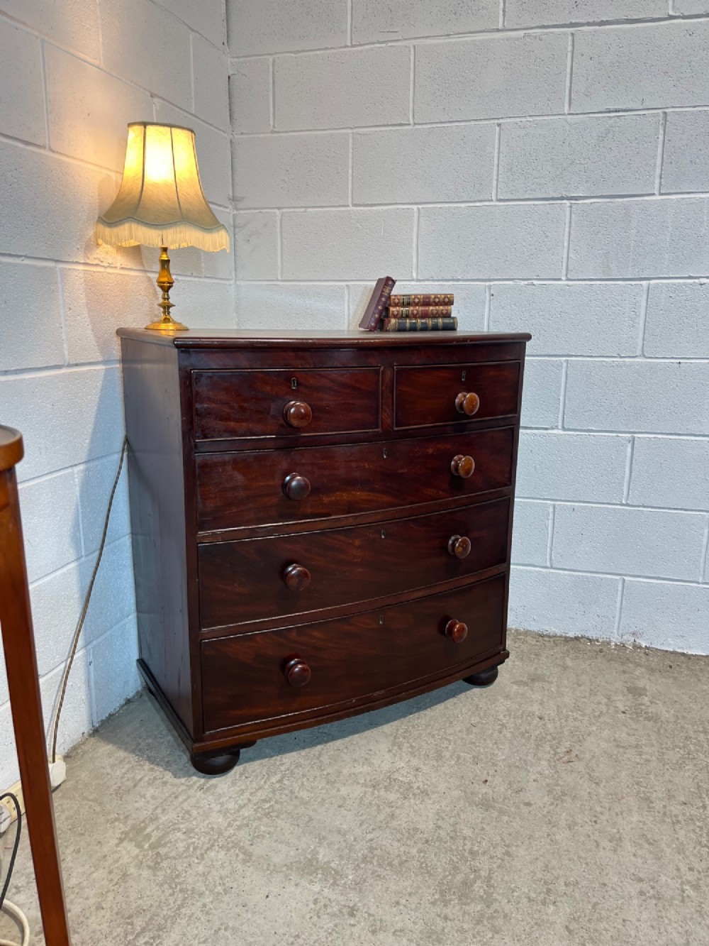 A 19th-century mahogany bowfront chest of drawers featuring two short drawers over three long drawers with turned wooden knobs and flame mahogany fronts.