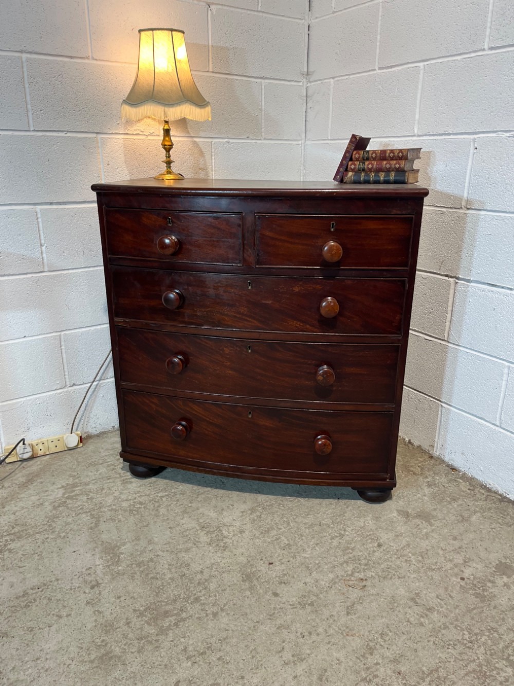 A 19th-century mahogany bowfront chest of drawers featuring two short drawers over three long drawers with turned wooden knobs and flame mahogany fronts. View IV