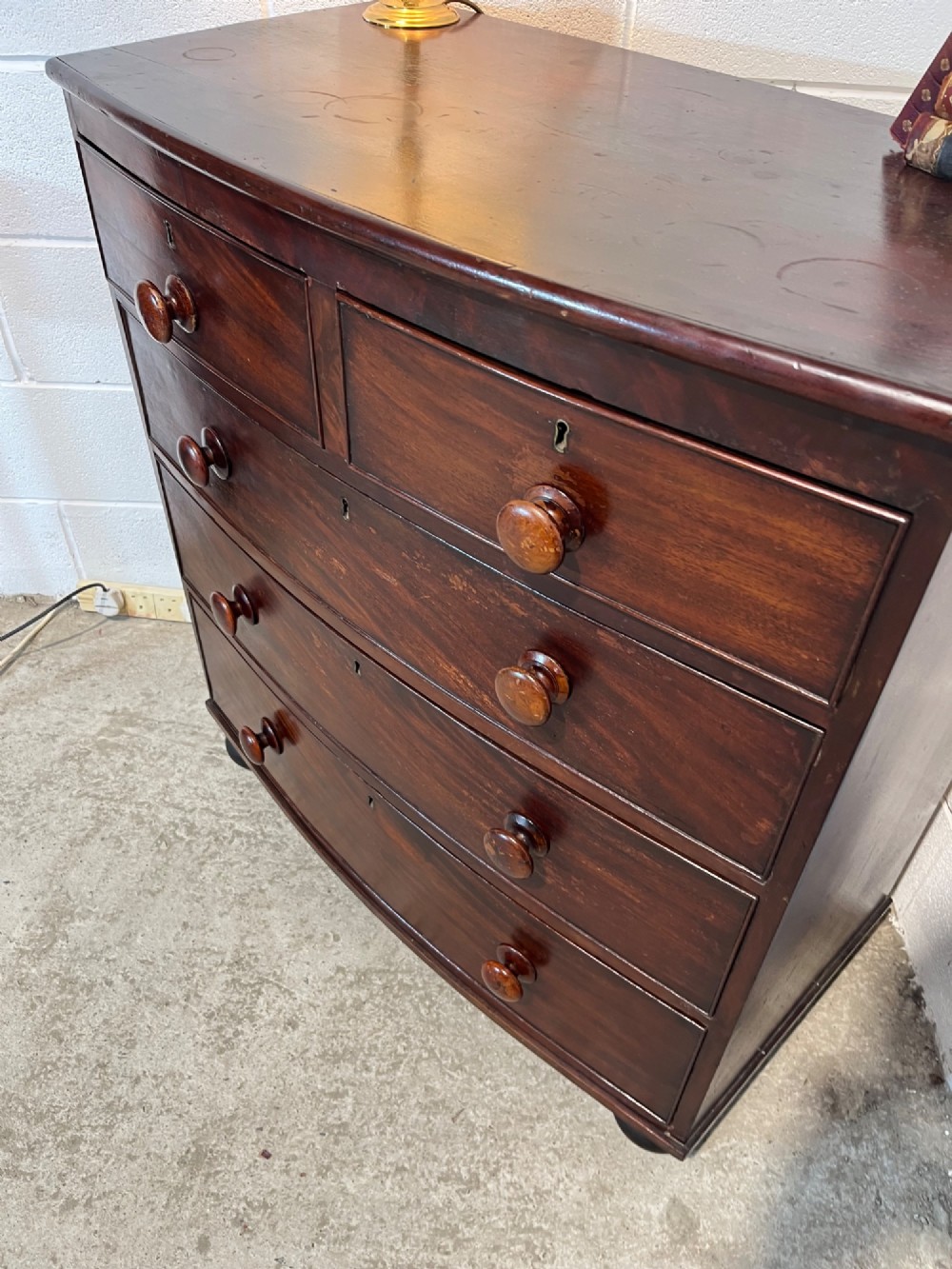 A 19th-century mahogany bowfront chest of drawers featuring two short drawers over three long drawers with turned wooden knobs and flame mahogany fronts. View VII