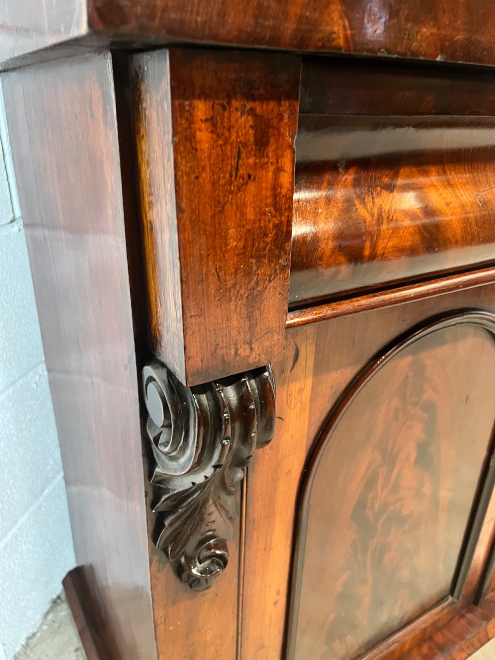 A 19th-century mahogany bookcase featuring two upper arched glazed doors displaying books, resting upon a lower two-door cupboard with flame veneer panels and carved scroll brackets. View IX