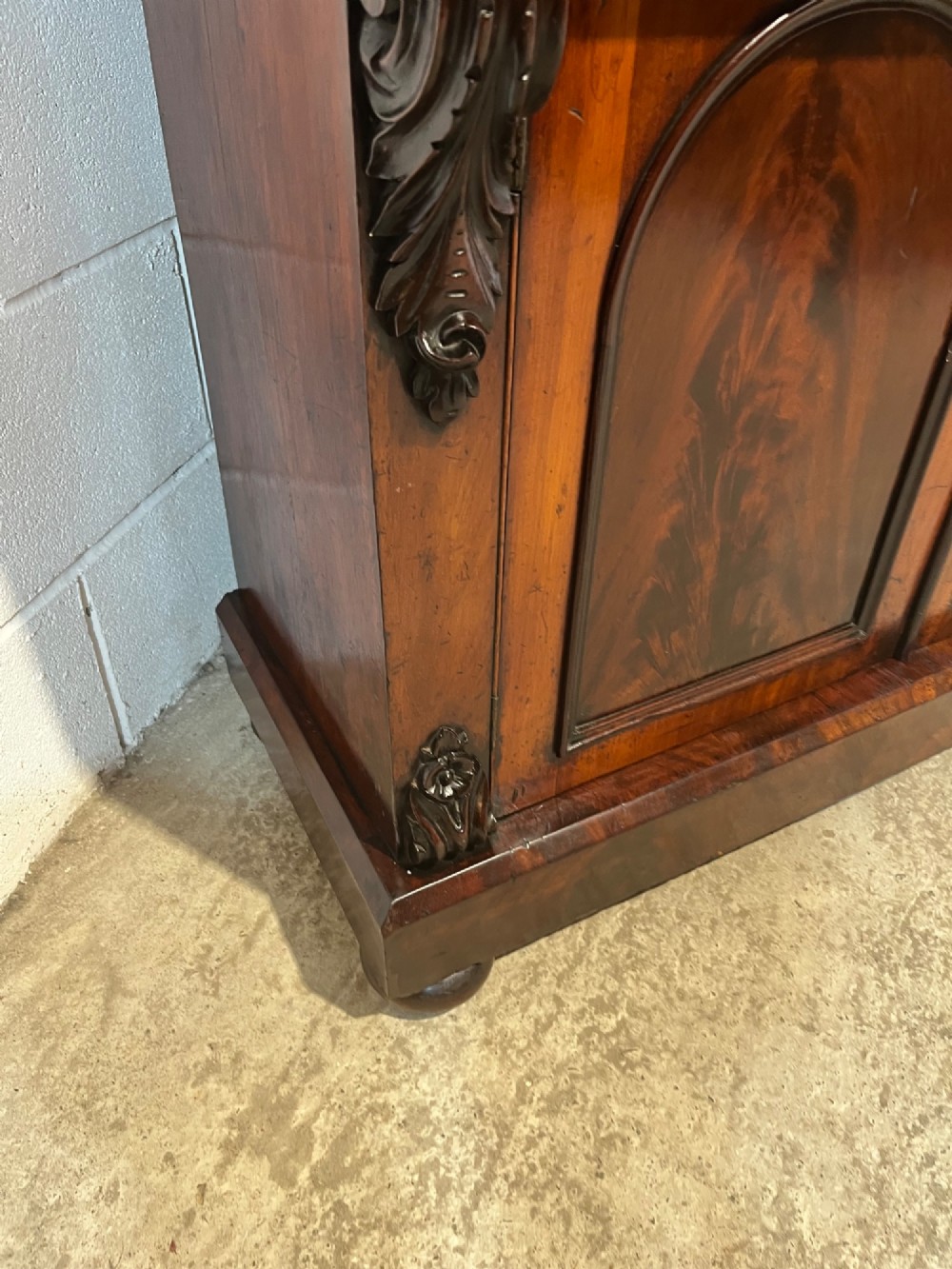 A 19th-century mahogany bookcase featuring two upper arched glazed doors displaying books, resting upon a lower two-door cupboard with flame veneer panels and carved scroll brackets. View X