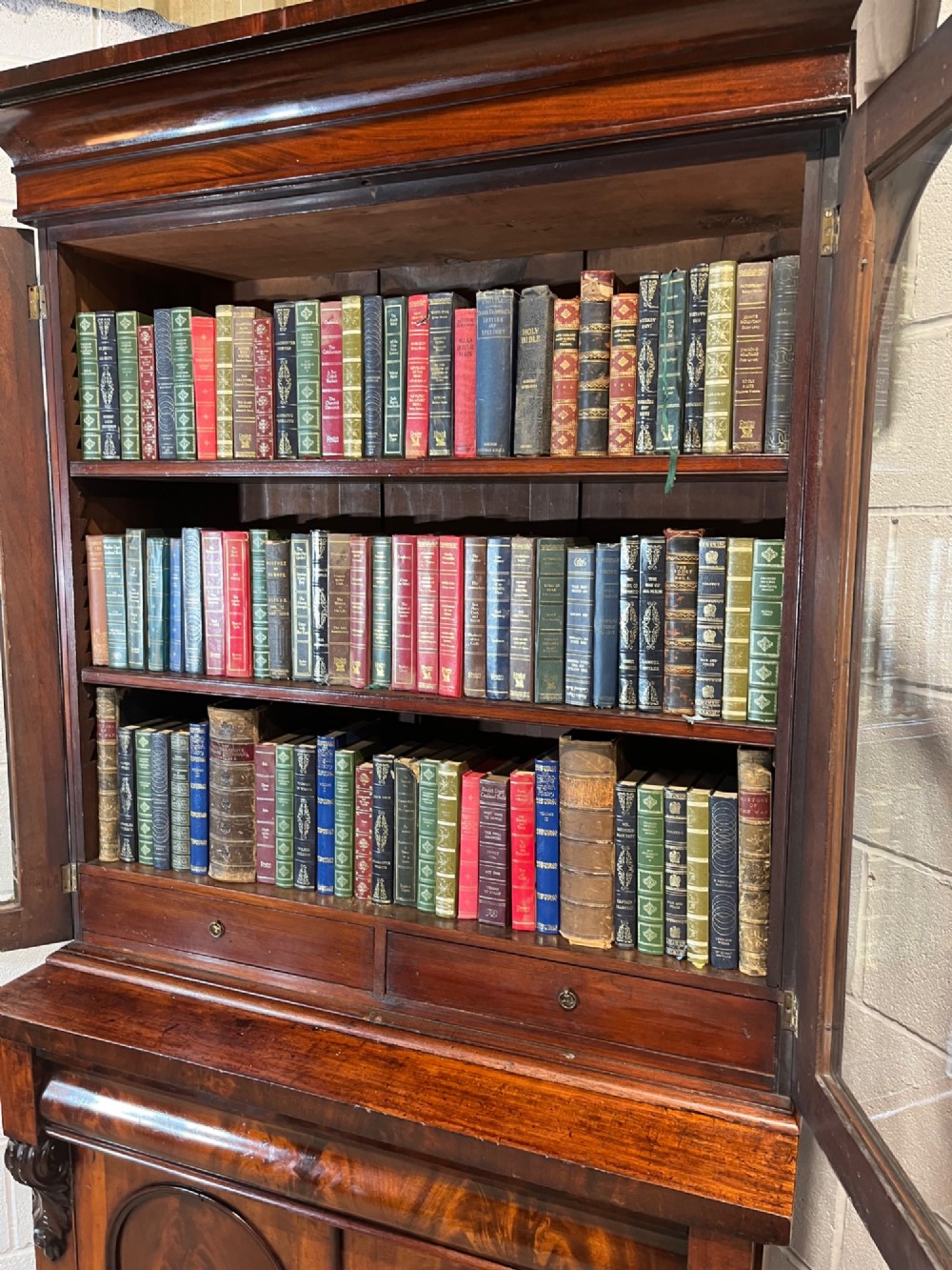 A 19th-century mahogany bookcase featuring two upper arched glazed doors displaying books, resting upon a lower two-door cupboard with flame veneer panels and carved scroll brackets. View XIII