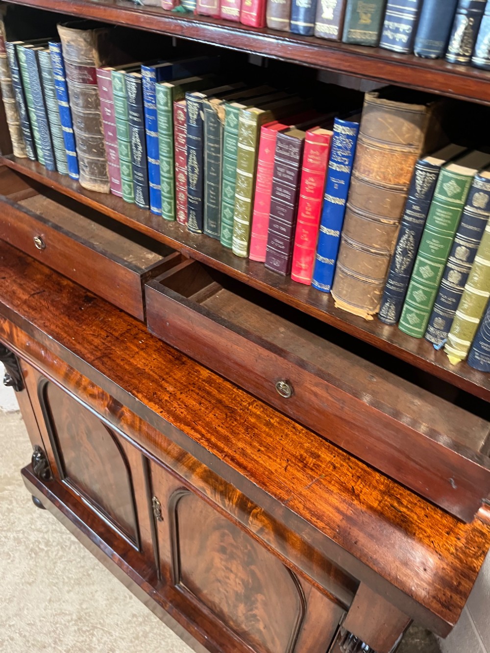 A 19th-century mahogany bookcase featuring two upper arched glazed doors displaying books, resting upon a lower two-door cupboard with flame veneer panels and carved scroll brackets. View XIV
