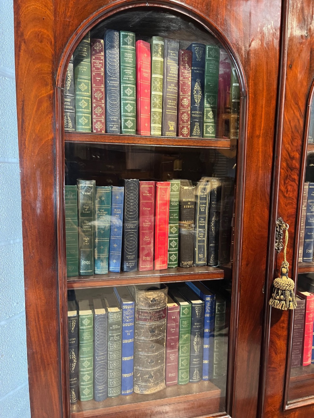 A 19th-century mahogany bookcase featuring two upper arched glazed doors displaying books, resting upon a lower two-door cupboard with flame veneer panels and carved scroll brackets. View XIV