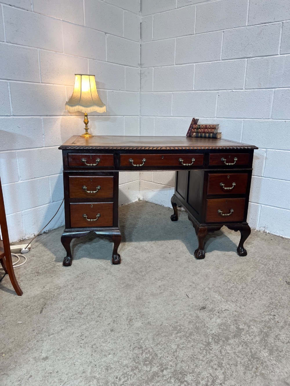 An early 20th-century dark mahogany pedestal writing desk featuring an inset leather top, brass swan-neck handles, seven drawers, and cabriole legs with ball and claw feet. View IV